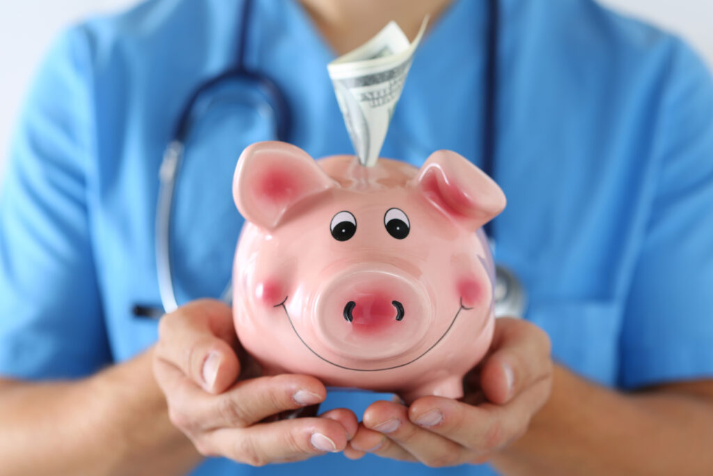 Nurse wearing blue uniform holding happy funny smiling piggybank in hands closeup. Money in slot. Focus on pig.